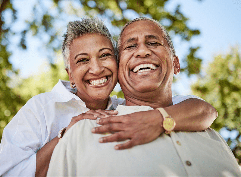 Happy mature couple smiling outdoors in sunny park setting with trees.
