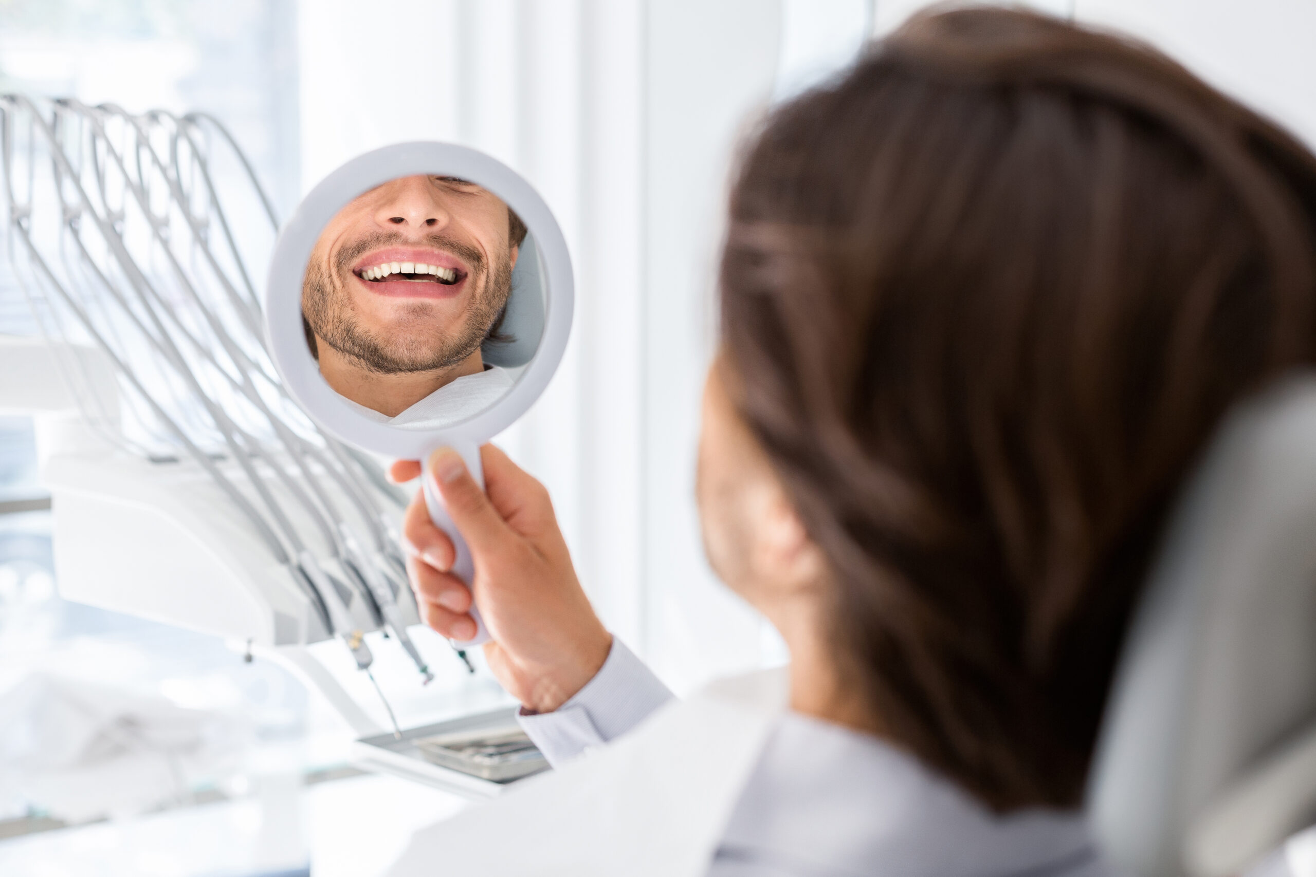 Satisfied patient checking smile at mirror in dental clinic Patient at a dental visit checking their smile in a mirror after treatment, reflecting improved comfort and reduced tooth sensitivity