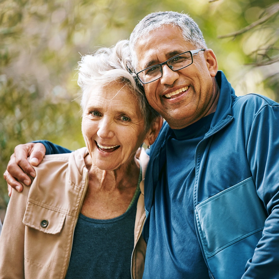 Happy mature couple smiling outdoors in sunny park setting with trees.