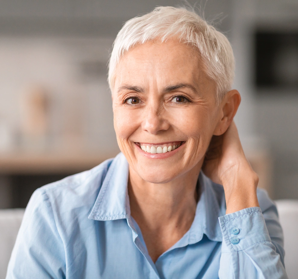 Smiling woman with long blonde hair resting head on arms against white background, dental clinic portrait.