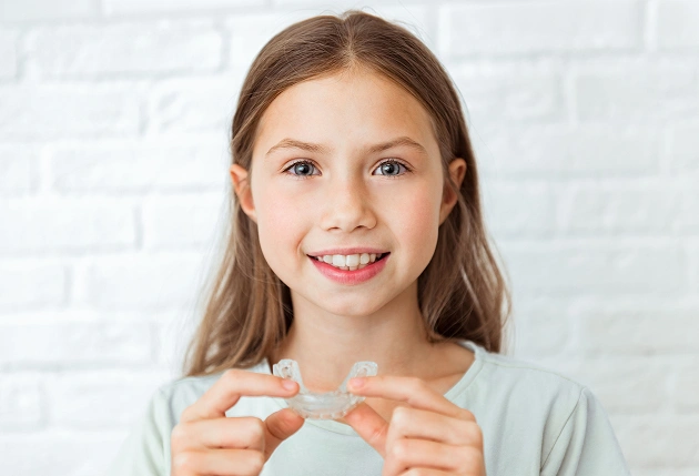 Smiling woman holding clear dental aligner or retainer in her hand indoors.