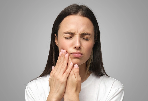 Woman holding cheek in pain, appearing to experience dental discomfort indoors.